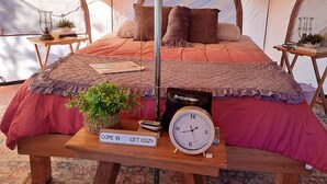 Una carpa con una cama, un reloj, un letrero y una pequeña mesa con una planta.