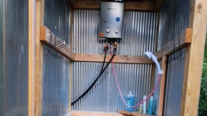 Un área de ducha pequeña y cerrada, con techo de metal, paredes de madera y un cabezal de ducha en la pared.