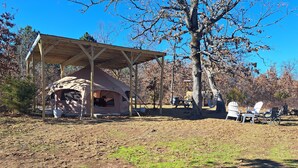 Un área de camping con tiendas de campaña y una zona de estar techada, con mobiliario exterior.