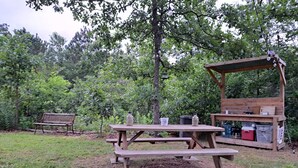 Un área de picnic con bancos y mesas de madera, rodeada de árboles.