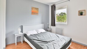 A bedroom with a bed, nightstands, a window with curtains, a radiator, and a wall-mounted picture. - Beautiful apart for 4 pers in the forest (Parentis-en-Born)