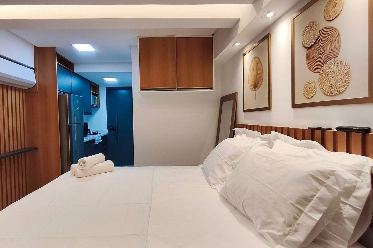 Quarto de hotel com cama, banheiro e cozinha compacta.