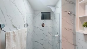 A bathroom with a glass shower enclosure, marble walls, and a white towel hanging on a rack.