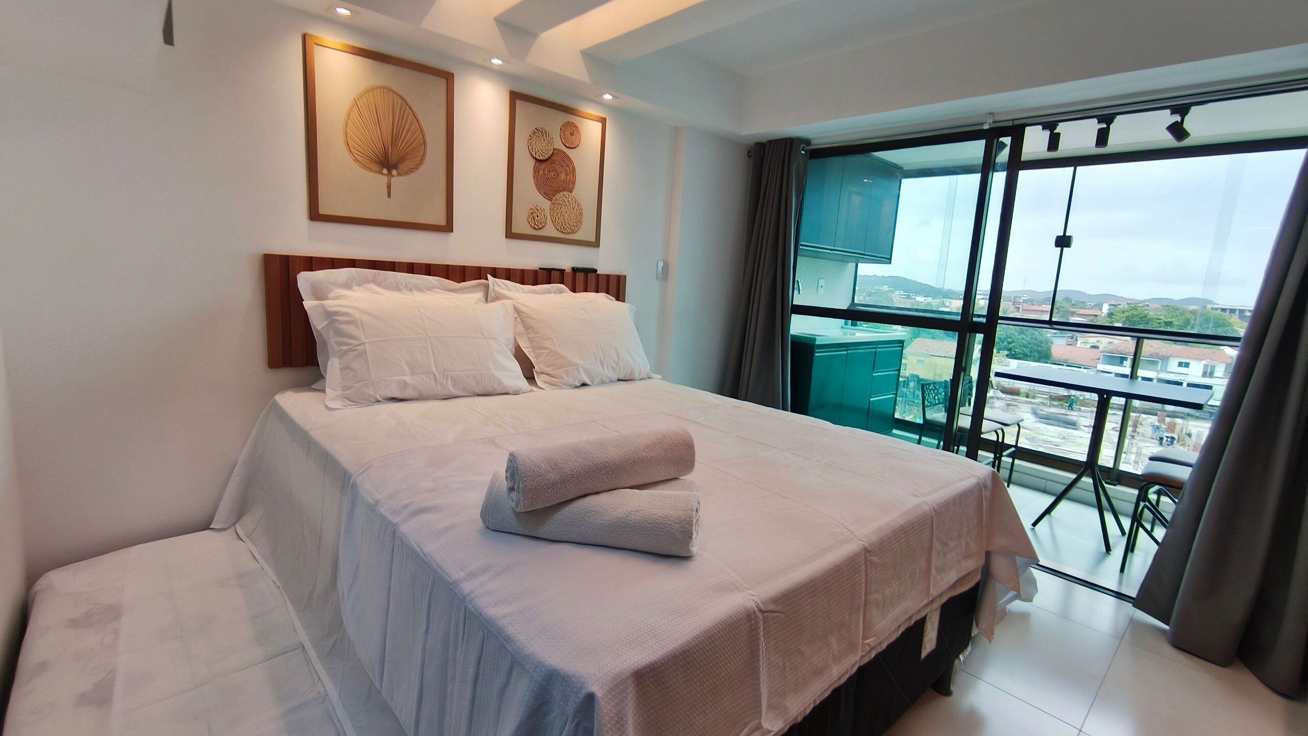 A hotel room with a bed, a balcony with a view, and artwork on the wall.