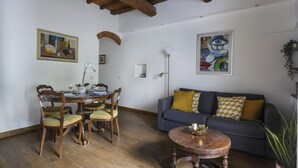 Een eethoek met een houten tafel en stoelen, een bank met gestreepte kussens, en een schilderij aan de muur.