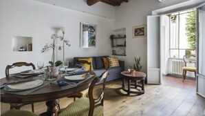 Een eetgedeelte met een houten tafel voor vier personen, een bank met kussens en een kleine ronde tafel met een plant.