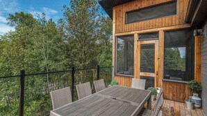 Una terraza de madera con una mesa y sillas, rodeada de árboles.