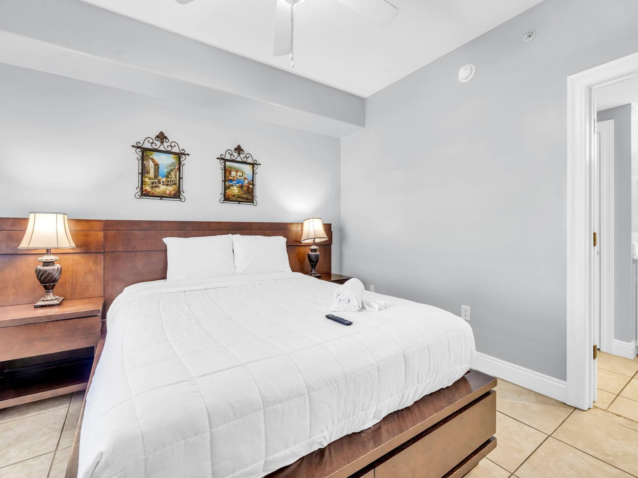 A hotel room with a large bed, two bedside lamps, a nightstand, and two wall-mounted paintings.