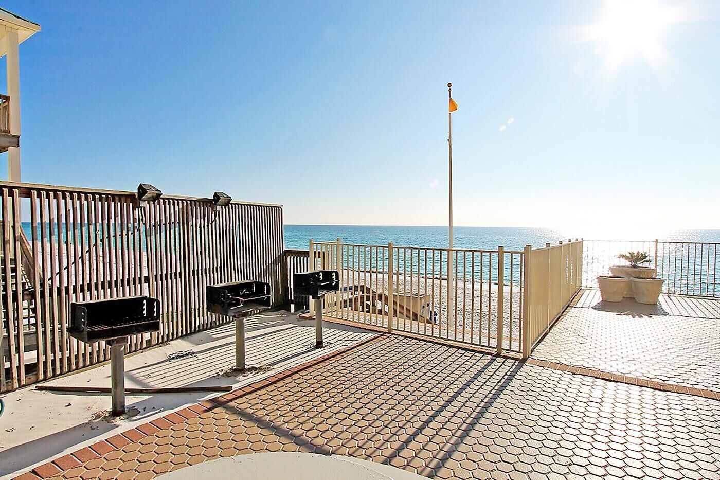 A beachside walkway with a metal fence, a flagpole, and potted plants.