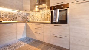 A modern kitchen with light wood cabinetry, patterned backsplash, stainless steel appliances, and a wooden floor.