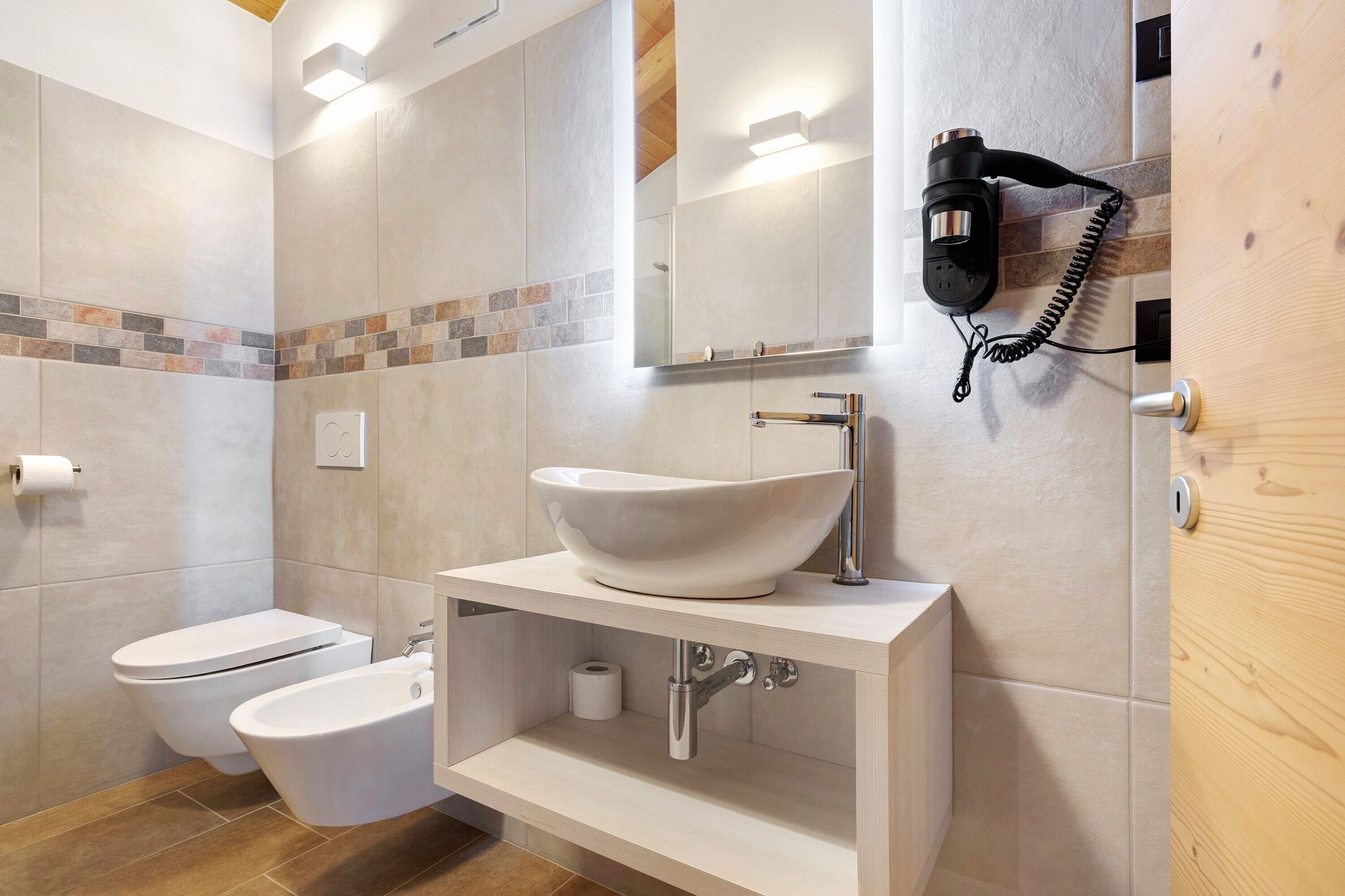 Un bany amb un rentapeus blanc, un vàter, un bidet, un penjador de tovalloles i un telèfon fixat a la paret.
