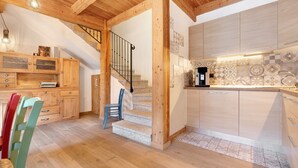 A modern kitchen with wooden cabinets, a staircase, and a dining area with chairs.