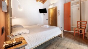 A bedroom with a bed, a TV, a wooden chair, and a wooden ceiling.