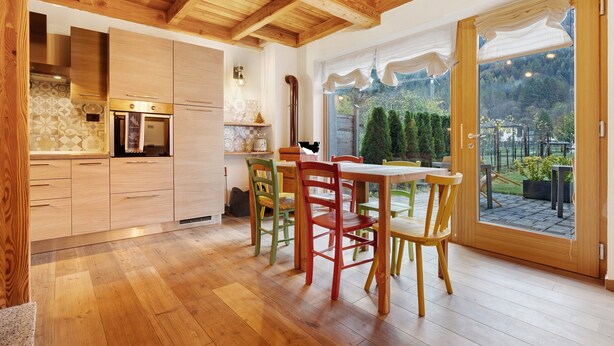 A kitchen with wooden cabinets, a dining table with chairs, and a view of the outdoors through a glass door.