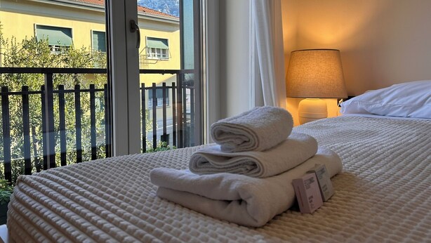A hotel room with a bed, a lamp, and a view of mountains through the window. - Centro Lecco [Dante Avenue]: Lake & Mountains (Lecco)