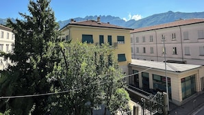 A building with a flat roof and a balcony, surrounded by trees and mountains in the background. - Centro Lecco [Dante Avenue]: Lake & Mountains (Lecco)