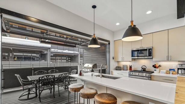 A modern kitchen with a large island, bar stools, and a dining area with a table and chairs. - Luxury 3BR Townhome with W/Private Spa 1089 (Steamboat Springs)