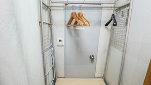 Una habitación pequeña y estrecha con un perchero metálico, perchas de madera y una puerta.