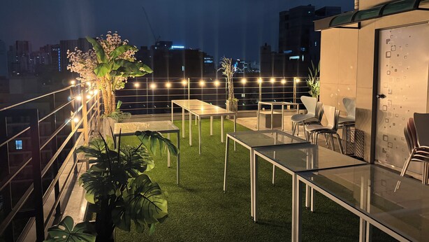 Una terraza en la azotea con césped artificial, mesas, sillas y luces colgantes.