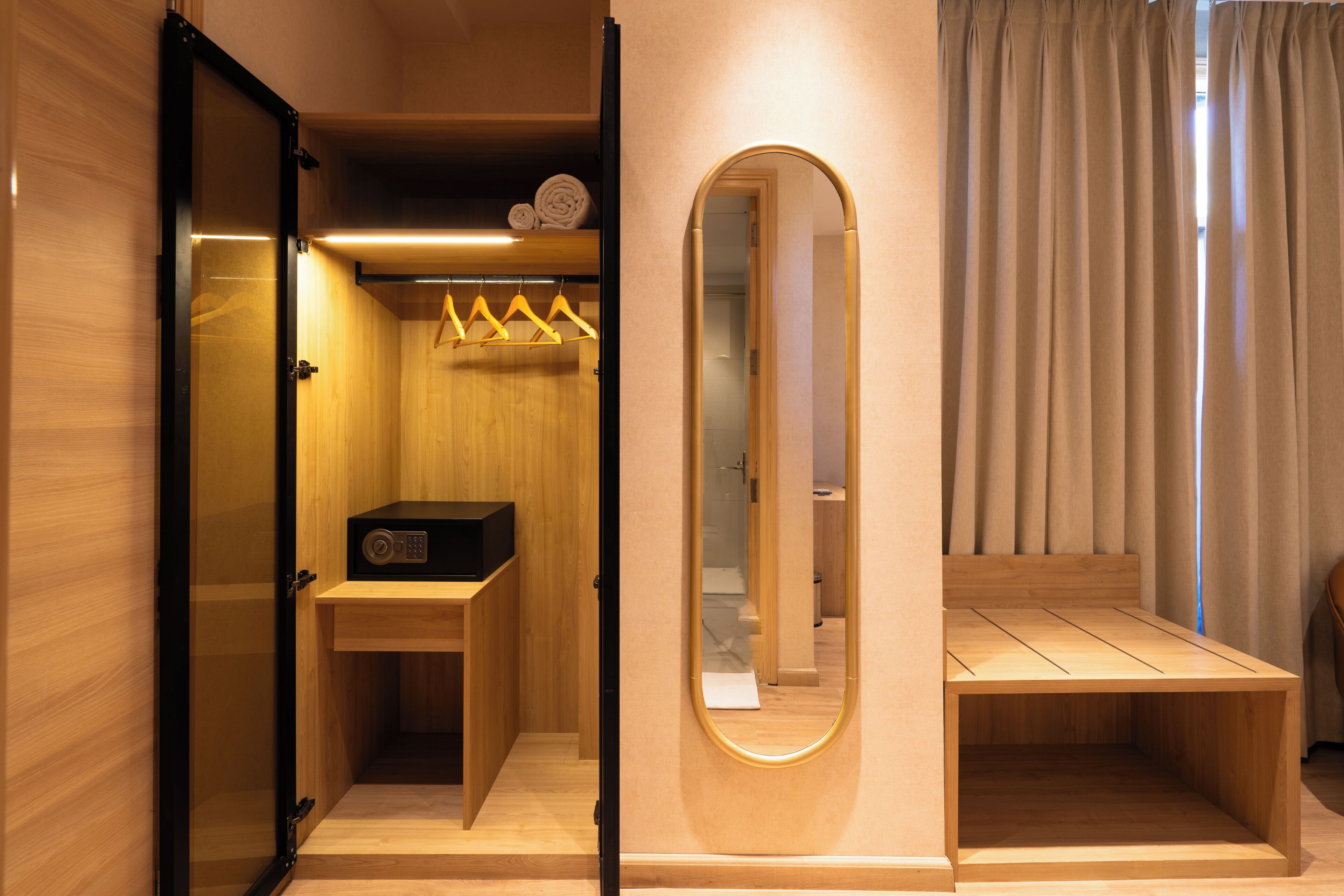 A compact room with a wooden wardrobe, a mirror, a small table, and a bench.
