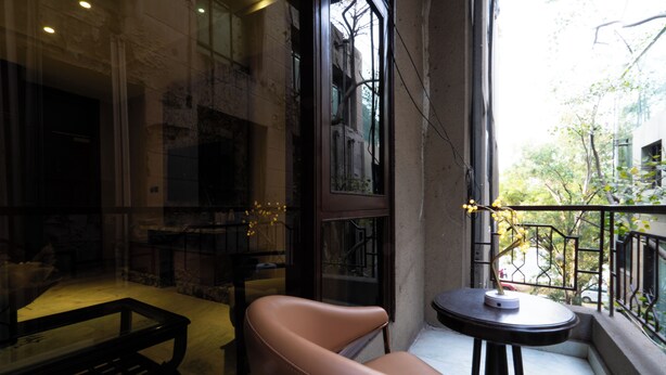 A modern interior with a leather chair, a small round table, and a view of the outside through a large window. - Hotel Bluestone Prime Nehru Place by The Cosy hotels (New Delhi)