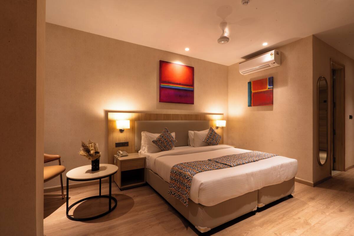 A hotel room with a bed, bedside tables, a chair, a small table with a vase, and artwork on the walls.