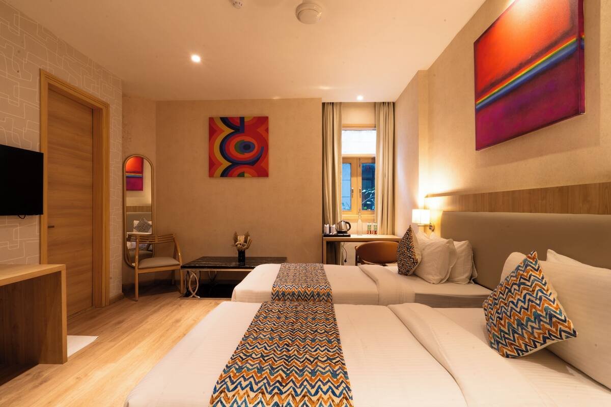 A hotel room with a bed, a desk, a chair, a TV, and artwork on the wall.