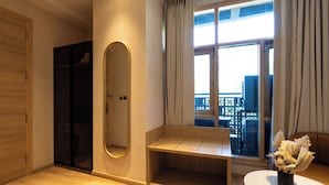 Ein Zimmer mit Holzboden, einer Bank, einem Spiegel, einem Fenster mit Vorhängen und Blick nach draußen.
