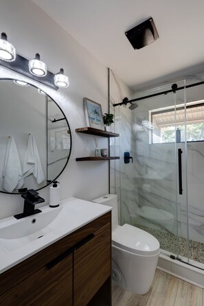 Et badeværelse med et stort spejl, en hvid vask, toilet og en brusekabine med glasvægge.