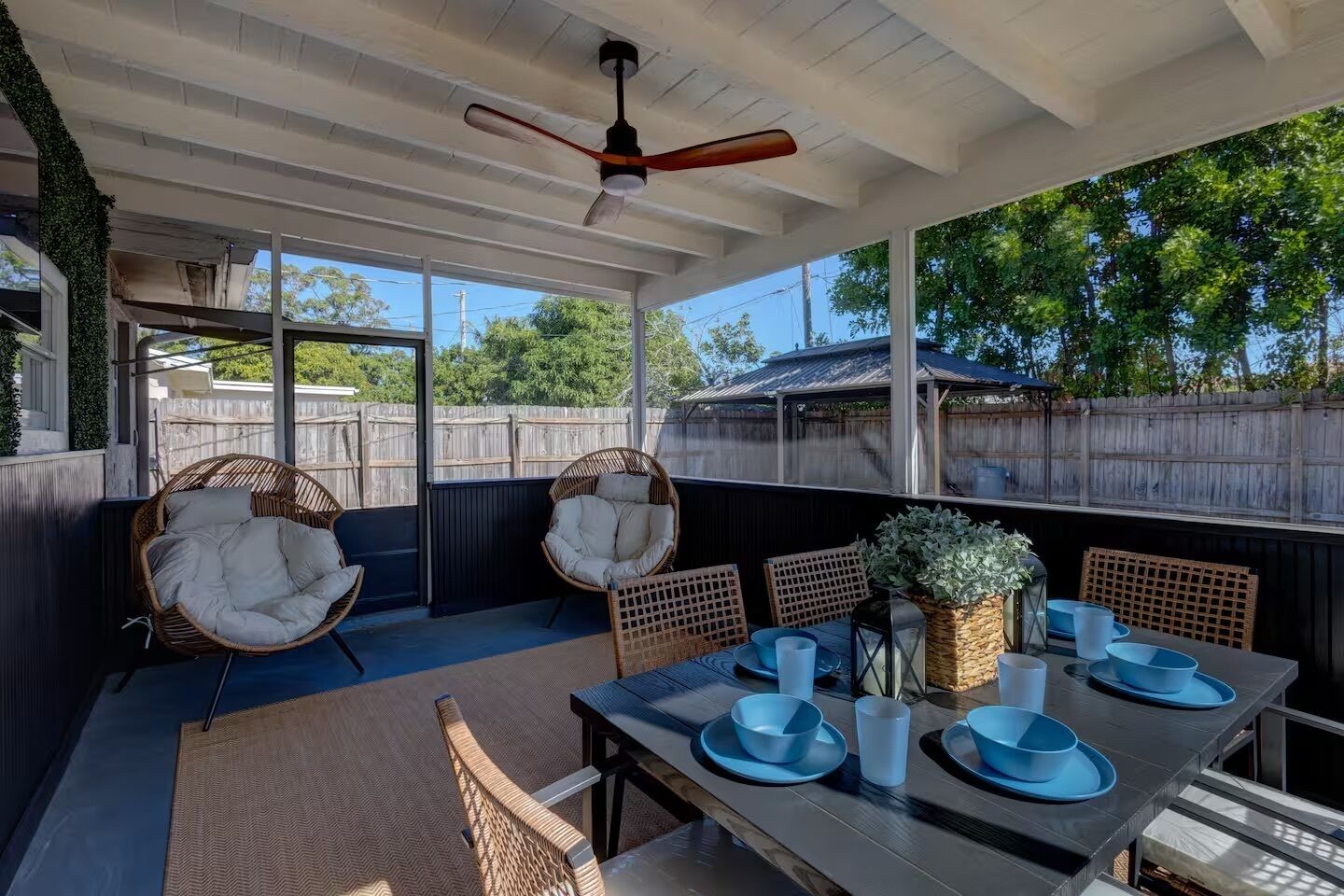 A covered patio with wicker chairs, a table set for dining, and a ceiling fan.