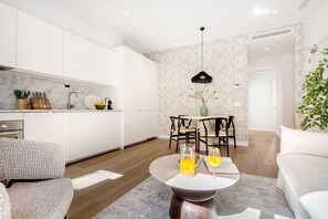 Una cocina moderna con armarios blancos, encimera de mármol y un comedor con mesa y sillas.