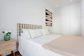 A bedroom with a bed, a bedside table, a vase with flowers, and a wall art piece.