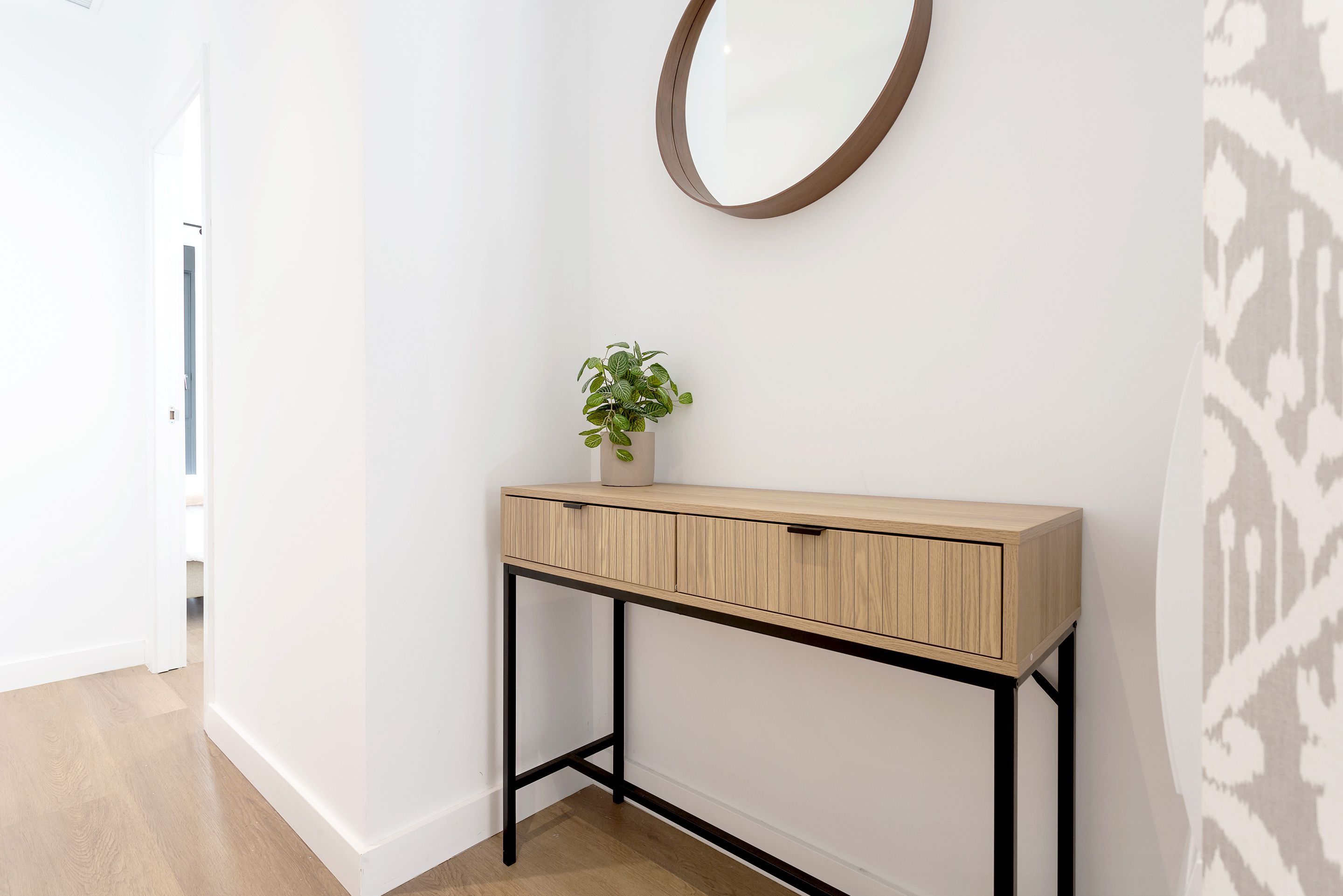 A hallway with a wooden console table, a potted plant, and a mirror on the wall.
