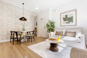 A modern living room with a dining area, a sofa set, a coffee table with croissants and juice, and a framed abstract painting on the wall. - Genteel Home Zabaleta I (Madrid)
