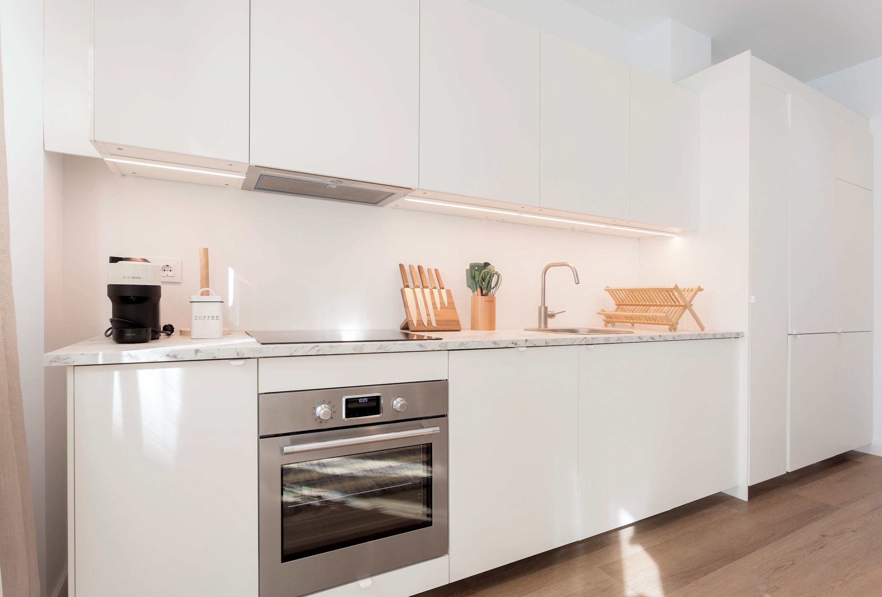 Une cuisine moderne avec des meubles blancs, un four encastré et une machine à café.