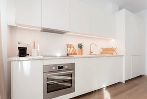 A modern kitchen with white cabinetry, a built-in oven, a coffee maker, and a wooden cutting board.