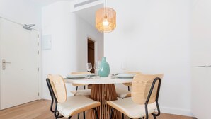 Een eetruimte met een ronde tafel, vier stoelen, een hanglamp en een blauwgroene vaas.