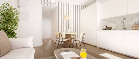 A modern living room with a sofa, a dining area with chairs, a kitchen with cabinets, and a decorative plant.