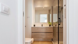 Een moderne badkamer met toilet, een houten wastafelmeubel, spiegel en een douchecabine van glas.