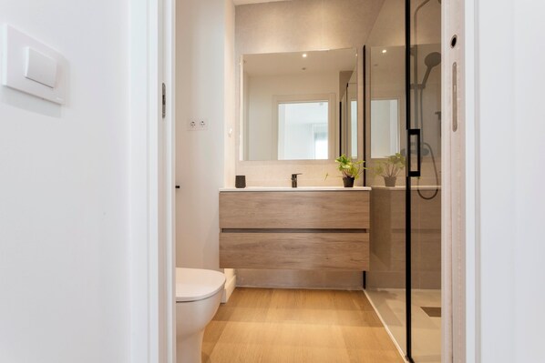 A modern bathroom with a toilet, a wooden vanity, a mirror, and a glass shower enclosure. - Genteel Home Zabaleta II (Madrid)