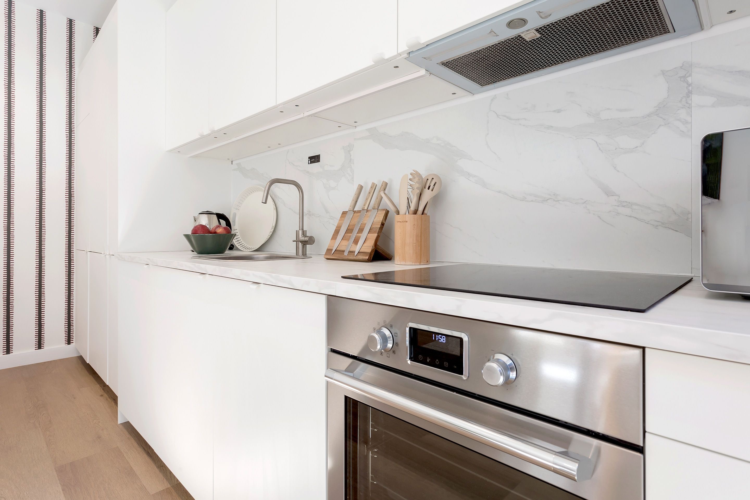 A modern kitchen with a stainless steel oven, a digital clock, and a knife block on the countertop.