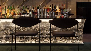 A bar area with two chairs, a variety of bottles, and a stone-tiled floor. - Íz Hotel Conceito (Goiânia)
