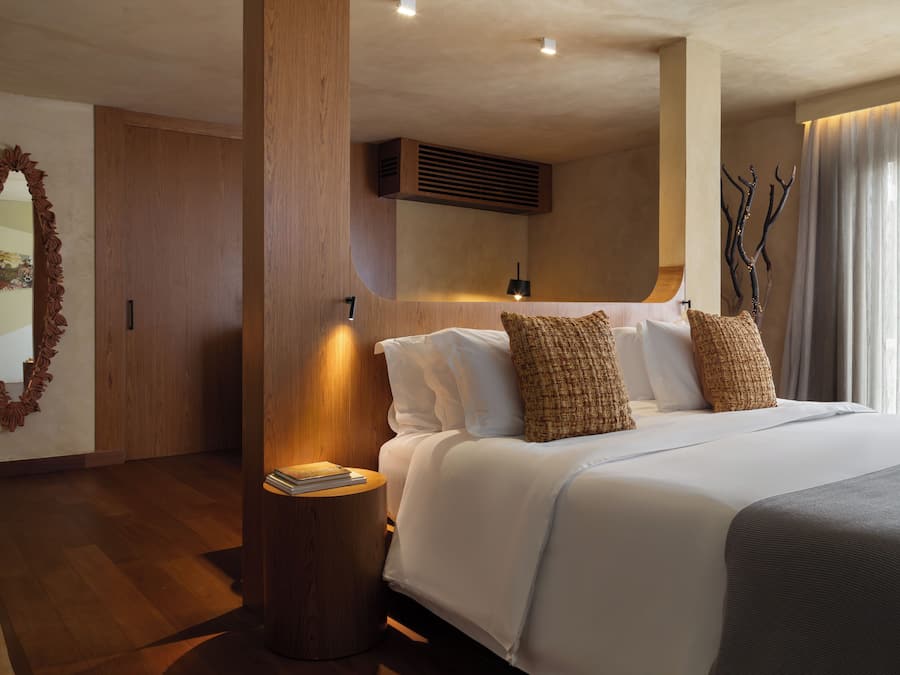 Una habitación de hotel moderna con una cama grande, cabecero de madera y un espejo decorativo.