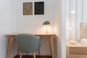 Une pièce comprenant un bureau en bois, une chaise verte, une lampe de bureau verte et une table de chevet avec un récipient blanc.
