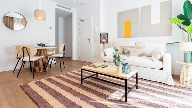 A modern living room with a striped rug, a white sofa, a dining area with chairs, and a coffee table. - Genteel Home Zabaleta III (Madrid)