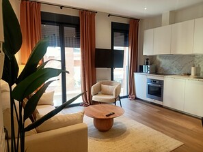 Una sala moderna con un sofá, una mesa de centro y un sillón. Cuenta con un área de cocina con armarios y un microondas.