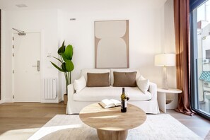 A modern living room with a white sofa, a round wooden coffee table, a potted plant, and a large abstract painting on the wall.