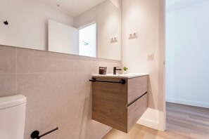 Une salle de bain moderne comprenant des toilettes, un meuble-lavabo en bois avec un évier et un miroir au-dessus du meuble.