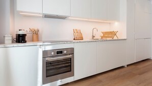A modern kitchen with white cabinetry, a built-in oven, a coffee maker, and a knife block.