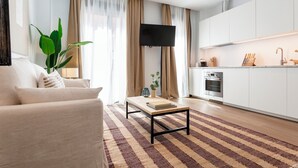 A modern living room with a sofa, a coffee table, and a TV. There is a kitchen area with cabinets and a stove. - Genteel Home Zabaleta III (Madrid)